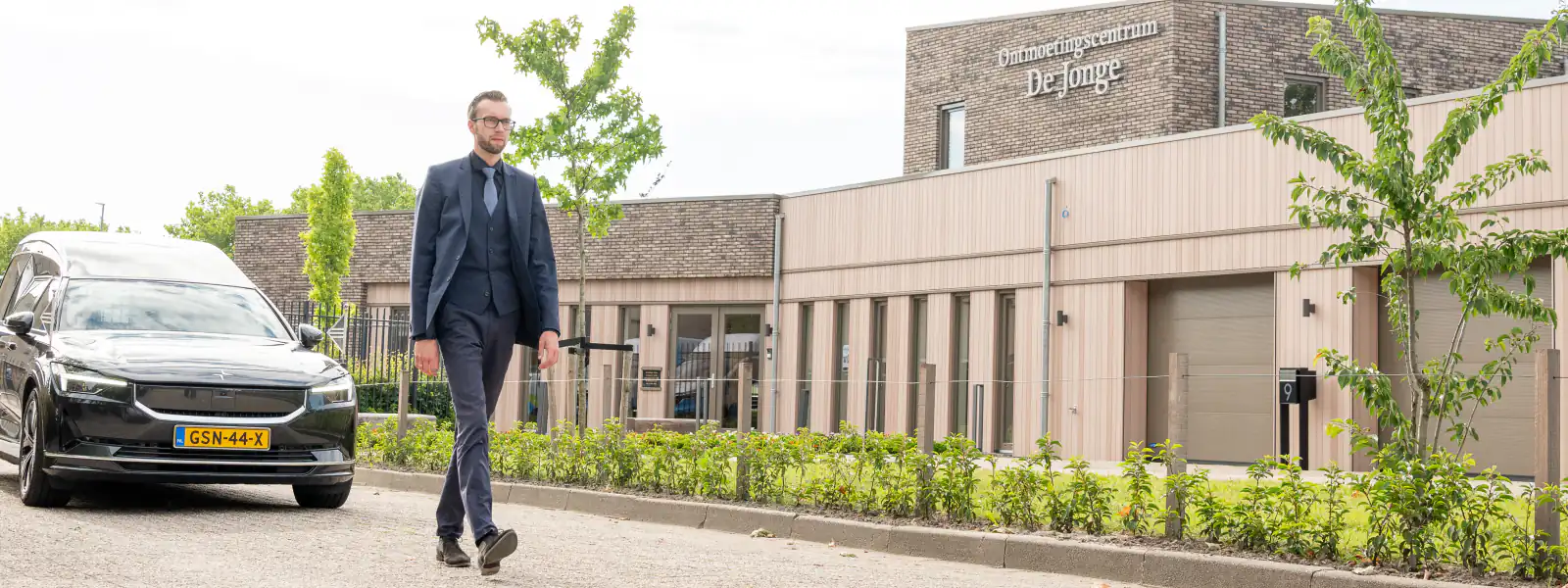 Een uitvaartverzorger loopt langs de rouwauto voor Ontmoetingscentrum De Jonge
